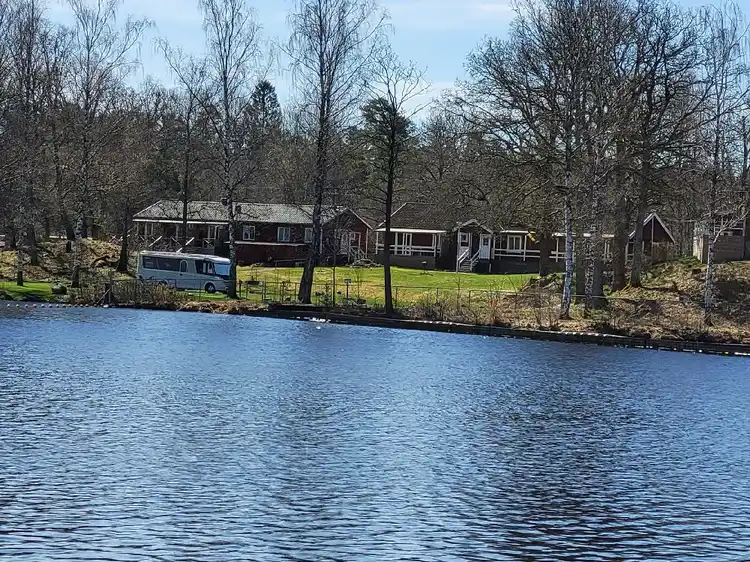 En lugn sjö omgiven av träd och natur, med spegelblankt vatten som sträcker sig genom landskapet vid platsen "den sovande älgen".