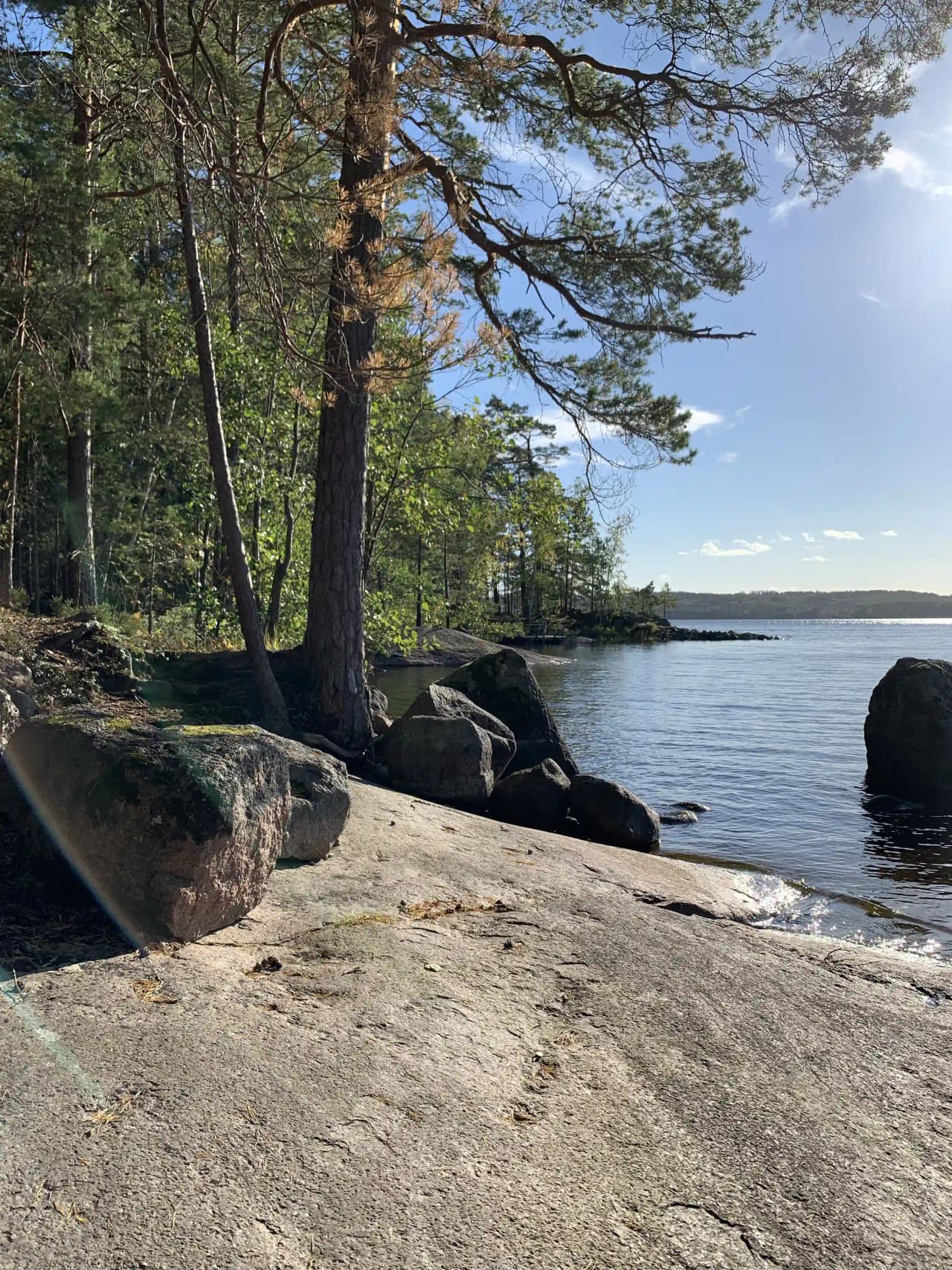En naturskön vy vid Hätte Camping med klippor och en kustlinje som möter en lugn sjö. Stranden ramas in av en vild och grönskande natur.