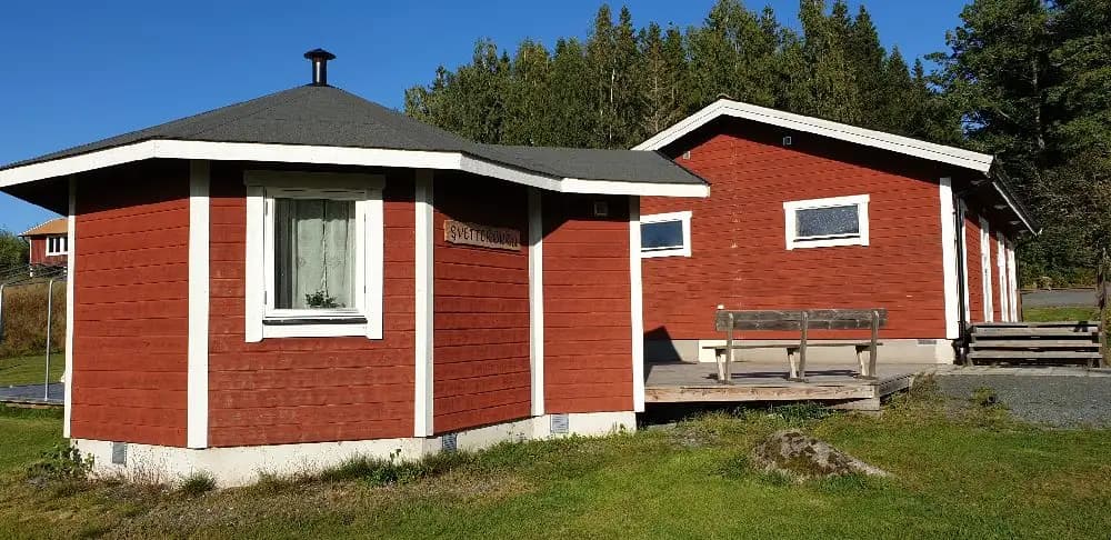 Alt-text: En trästuga med sluttande tak och dörromgivning i Målsånna Camping Park.