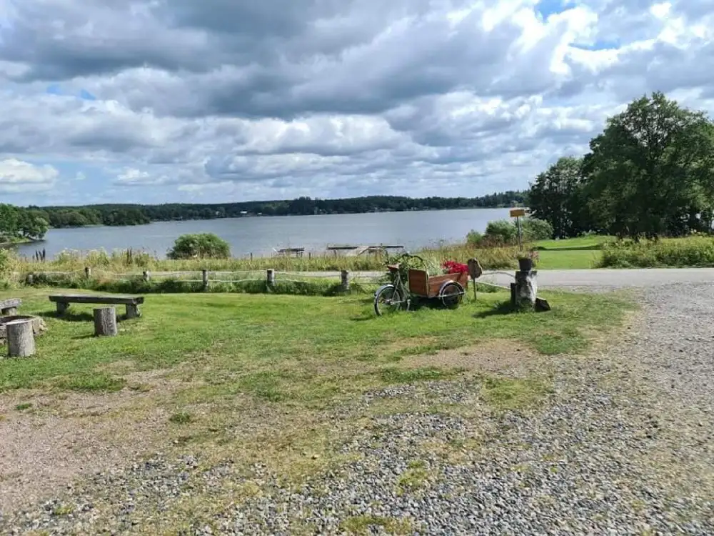En vidsträckt gräsyta med utsikt över en himmel fylld med moln. I bakgrunden syns vatten som sträcker ut sig mot horisonten, vilket skapar en lugn och naturskön atmosfär. Platsen är Säms Camping och Café.
