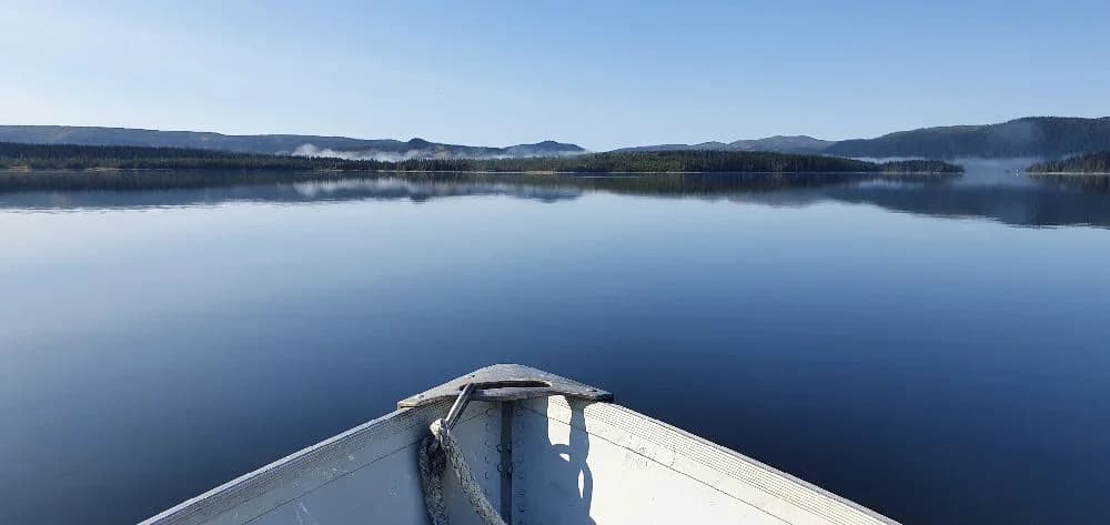 En vacker vy över Jormvattnets Fiskecamp med klarblå himmel och vita moln speglade i det stilla vattnet.