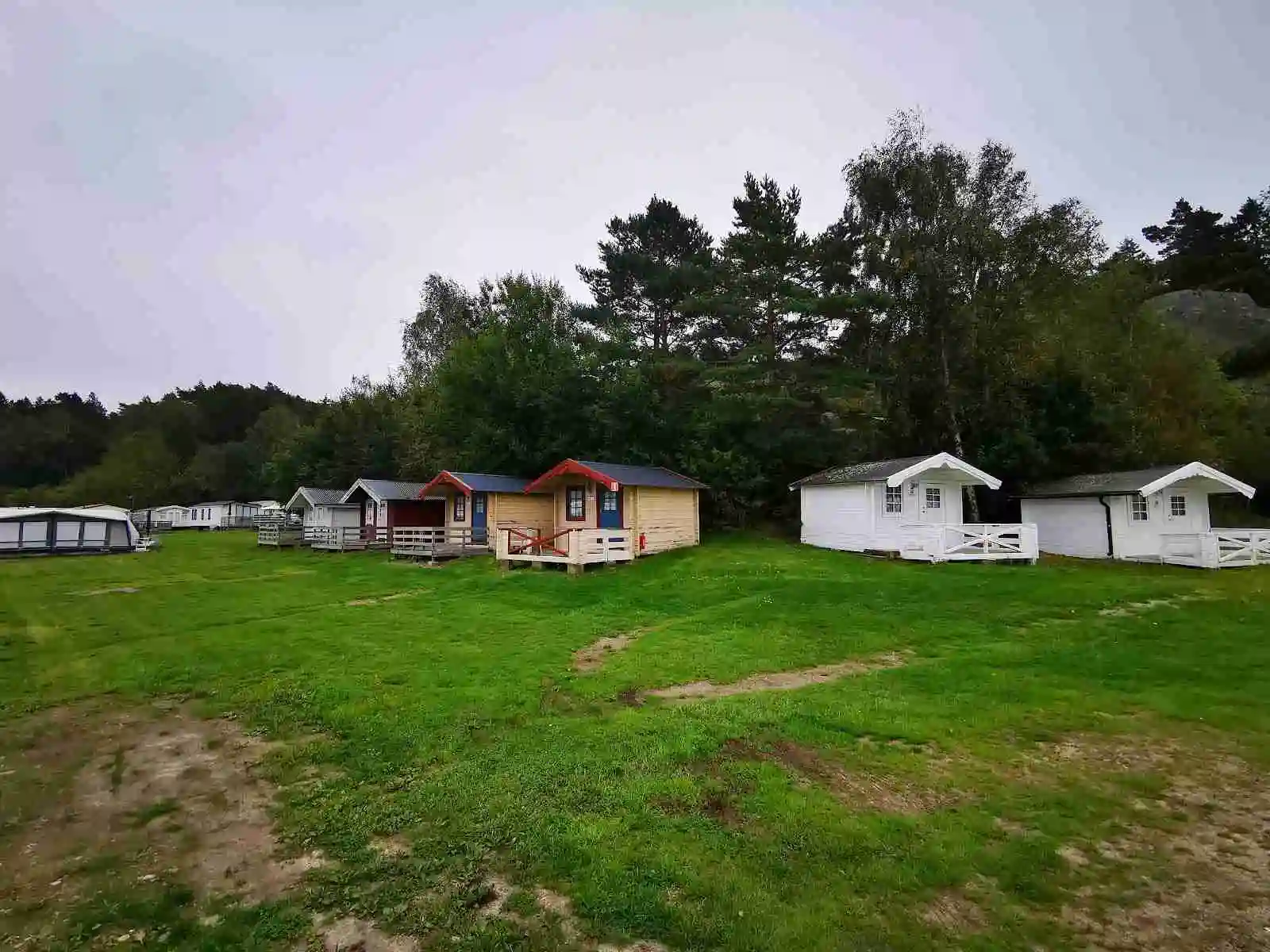 En grönskande park med en log cabin och ett tält under en himmel med cumulusmoln på Hunnebostrands camping och stugor.