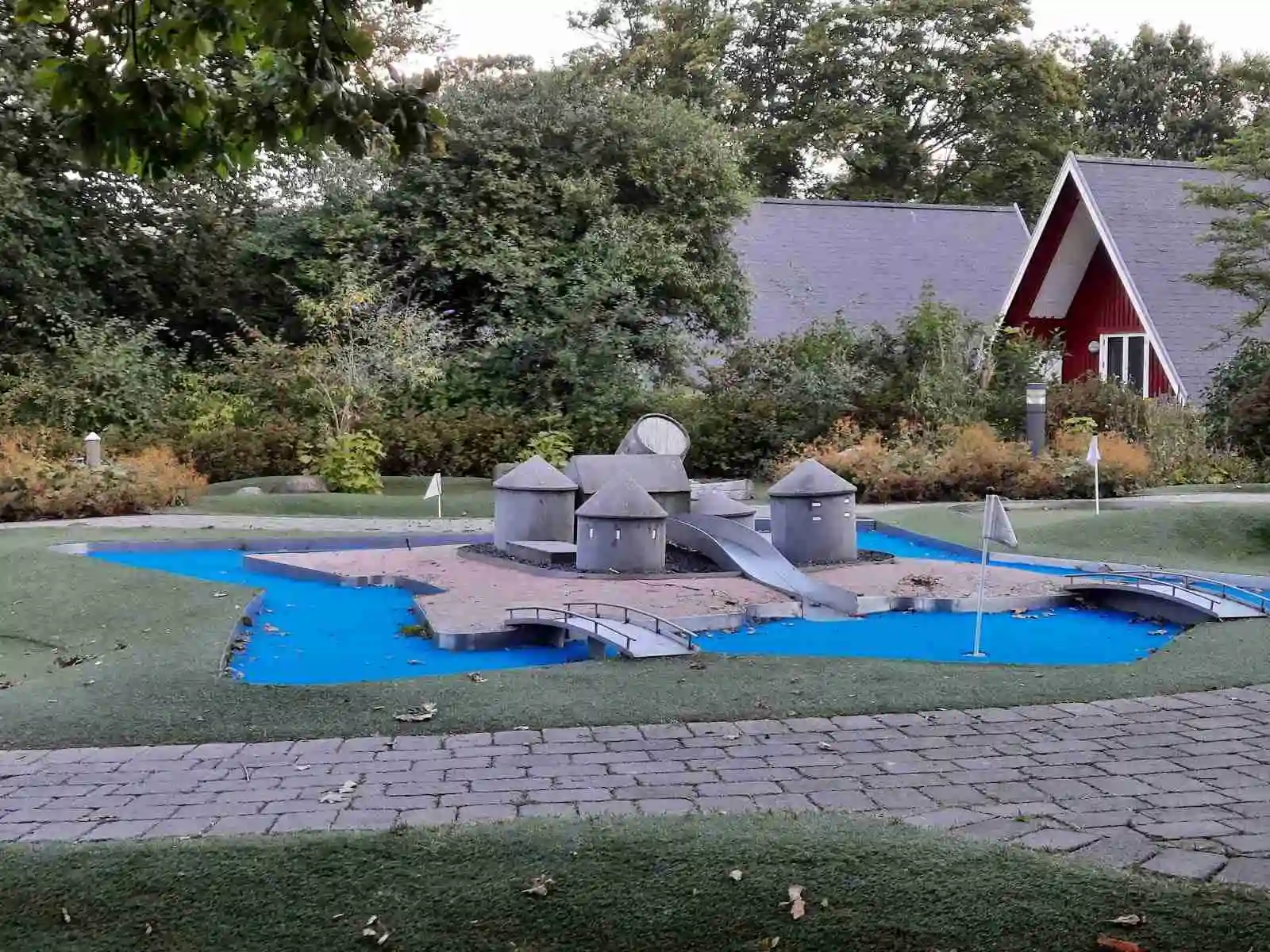 En grönskande park vid mötesplats Borstahusen med gräsmattor och trädgårdslandskap. Lekutrustning för barn finns tillgänglig och en uppfart leder genom området, som är inbjudande för rekreation och avkoppling.