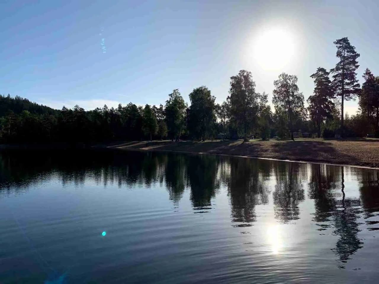 En naturskön vy över en sjö vid Pinnarp Camping, med blå himmel, klart vatten och omgivande träd.