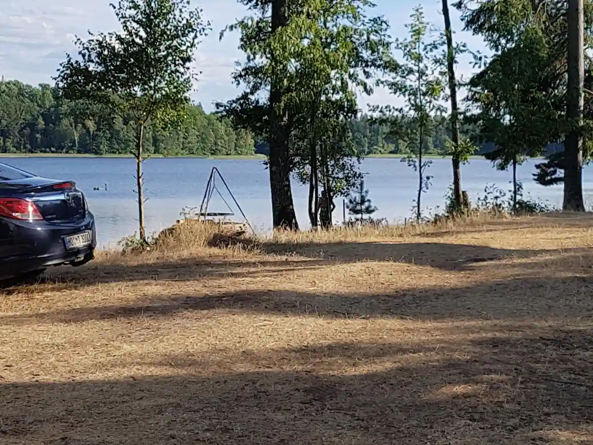 En lyxbil står parkerad vid en strandnära plats vid Hallsjö vildmarkscamping. Bakgrunden visar en vacker reservoar omgiven av natur.