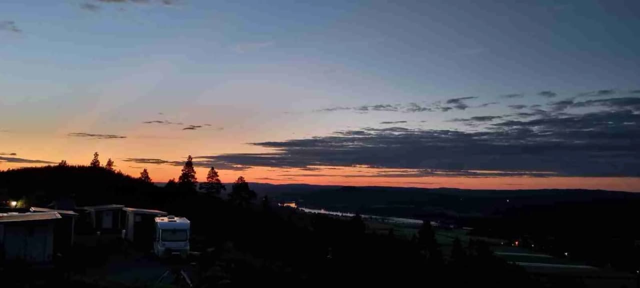 En stämningsfull vy över horisonten vid Järvsö Bergscamping, där himlen färgas av solnedgångens efterglöd.