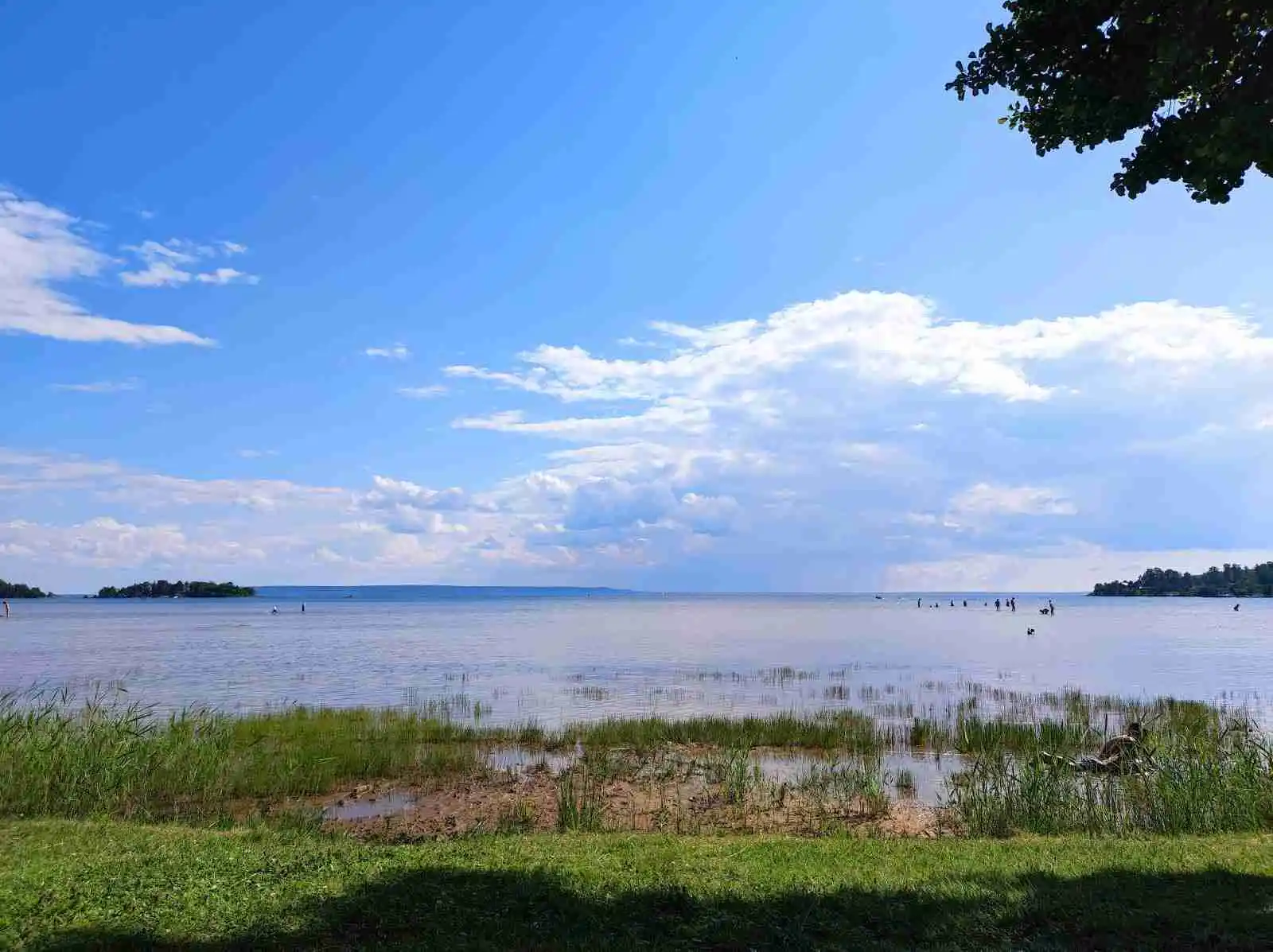 En klarblå himmel speglas i ett stilla vattendrag vid Sikhalls camping, med några lätta moln på himlen och en horisont i bakgrunden.