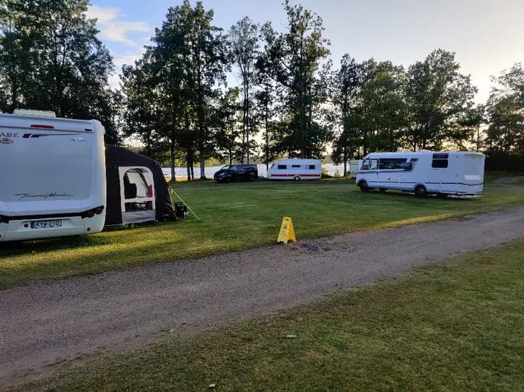 En husvagn och en skåpbil parkerade på en campingplats, omgivet av natur med träd och grönska i bakgrunden.