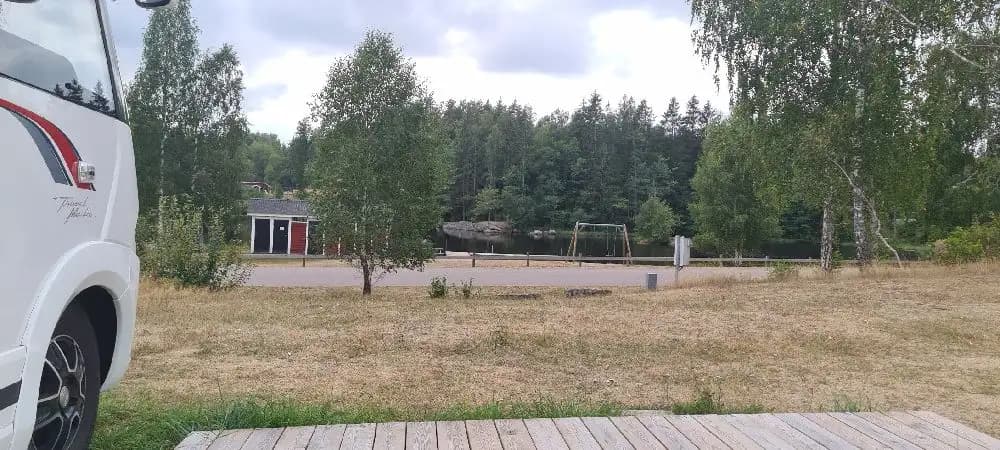 Bild av Broakulla Ställplats & Camping med en asfalterad uppfart där flera fordon är parkerade, inklusive en skåpbil och en SUV. Området verkar vara ett populärt ställe för husbilar och camping, med gott om parkeringsplats för besökare.