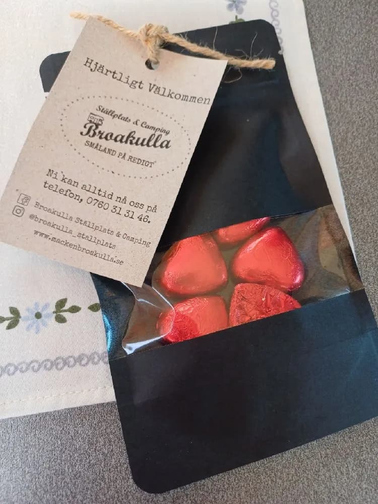 En packe färska jordgubbar med gröna kvistar och etikett, redo att säljas som lokalproducerad frukt vid Broakulla ställplats & camping.