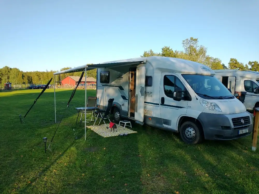 En husbil och en cykel parkerade på en campingplats, omgivna av tält och tarpar, med en avslappnad utomhusmiljö på Broakulla ställplats & camping.