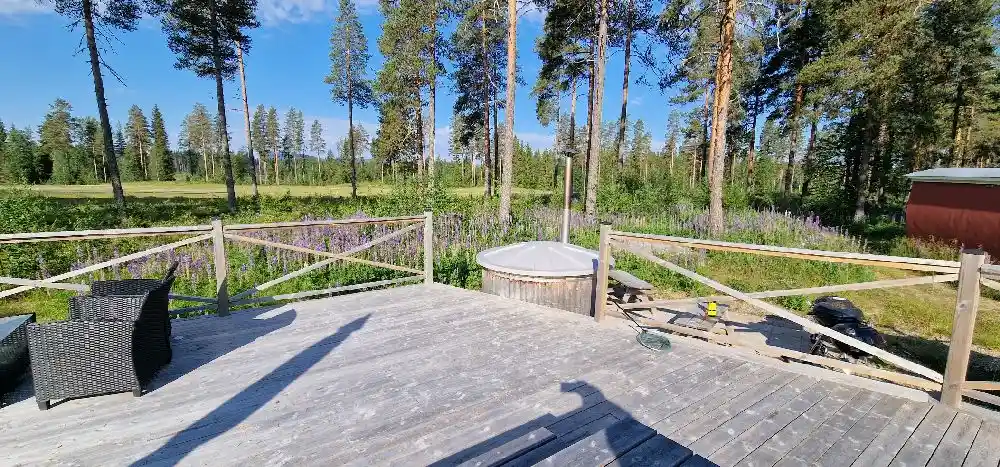 Bild av en träveranda med plankgolv och ett staket, omgiven av grönska, på Bjurholms camping.