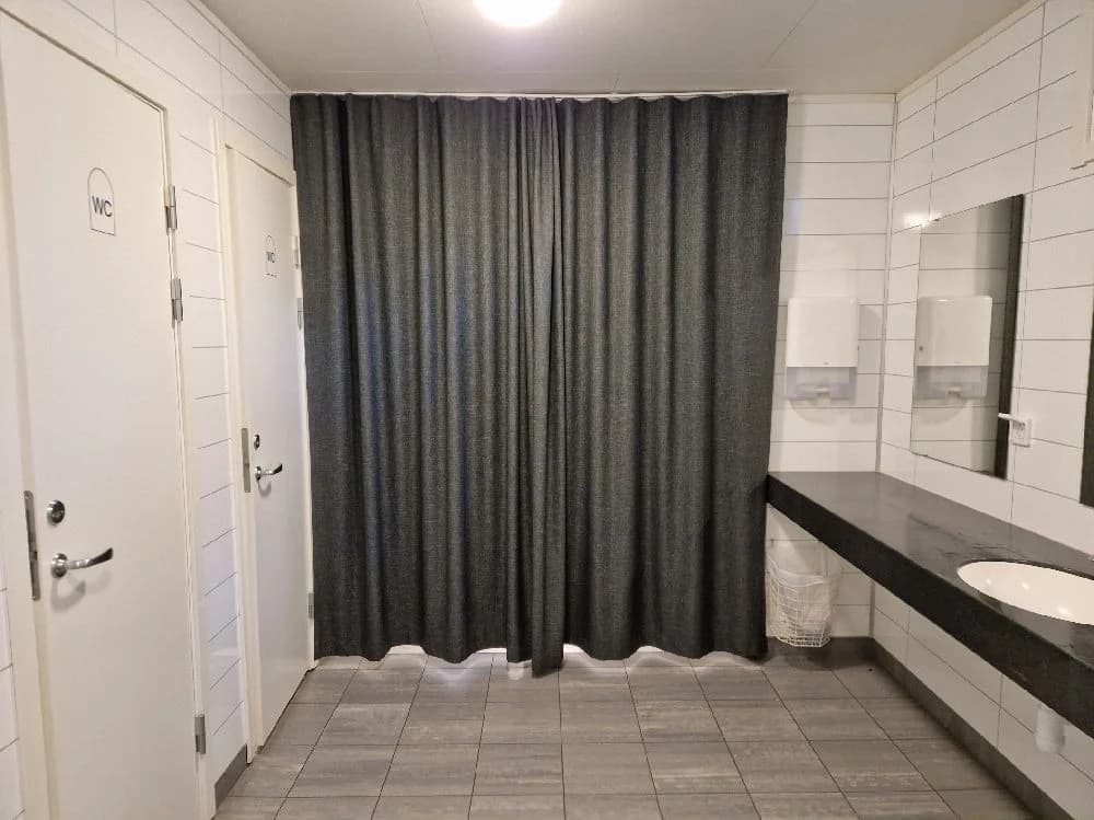 En stilfullt designad grått kaklat badrum med eleganta silverfärgade VVS-armaturer och ett draperi vid duschen på Isaberg Mountain Resort.