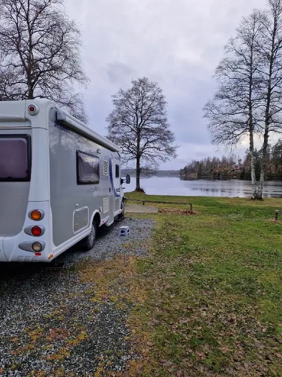 En husvagn står parkerad på en campingplats vid Ragnerudssjöns camping och stugby, omgiven av grönska och natur.
