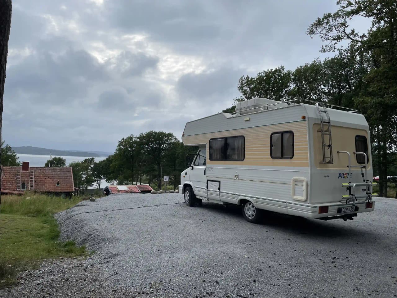 En husbil och en husvagn står parkerade på en campingplats vid Stenungsögården, omgiven av grönska och träd.