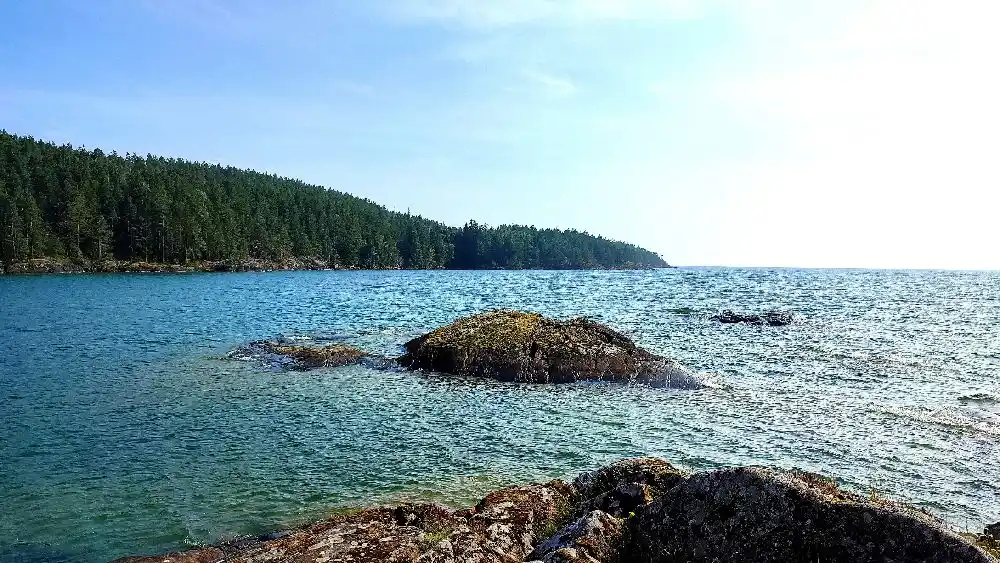 En naturskön vy över Harge bad & camping med blått vatten, klippor och kustlandskap. Somrig atmosfär med en känsla av vildmark.