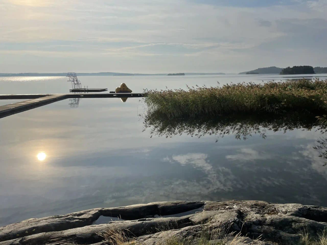 En vacker vy över en lugn sjö vid Björknäs camping, med glittrande vatten och en horisont av skogsklädda kullar som reflekterar i ytan.