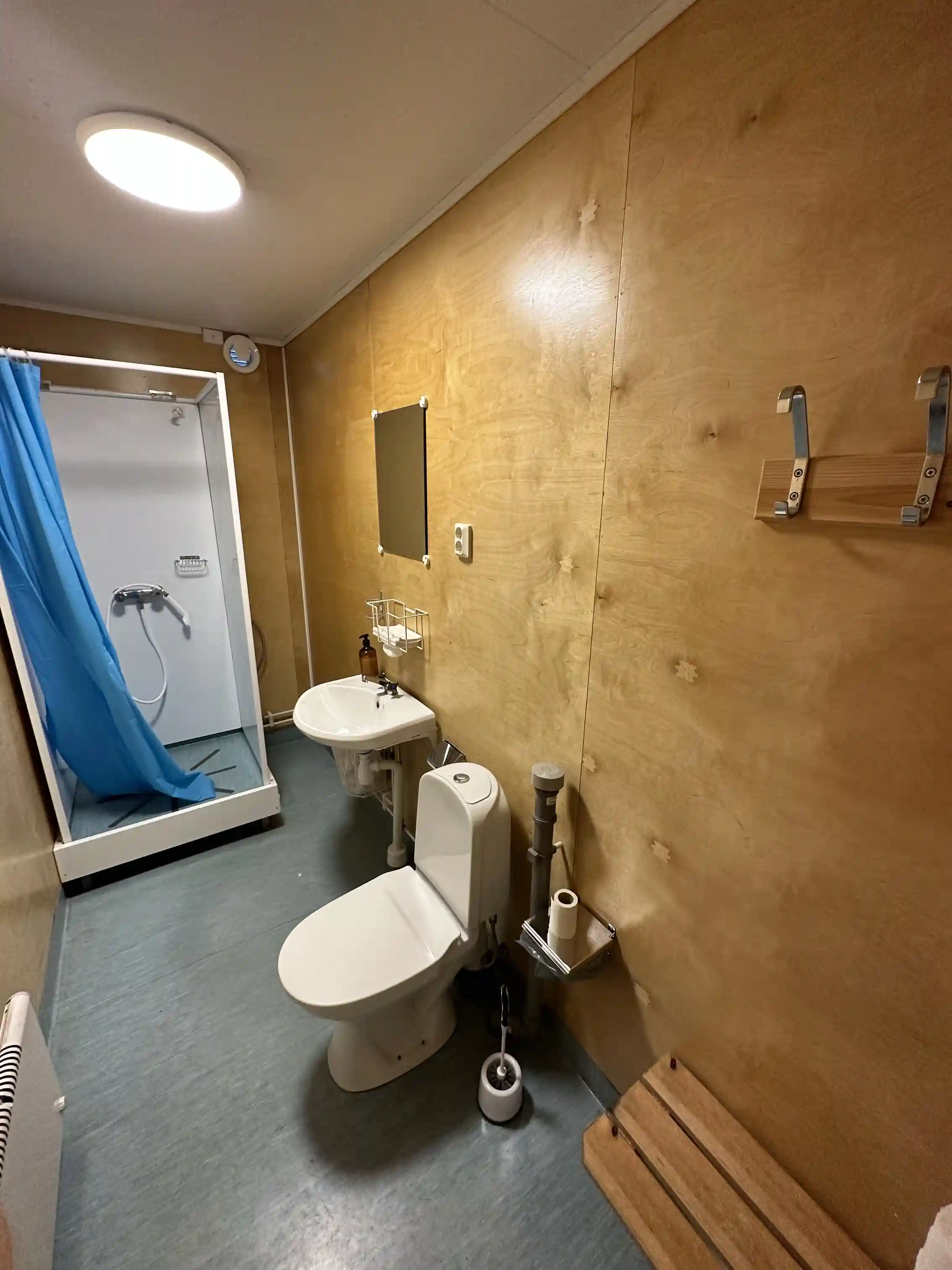 Bilden visar ett badrum på Björknäs camping med ett modernt och rent utseende. Inredningen består av ett handfat, en toalett med sits och trädetaljer. Väggarna och golvet är kaklade.