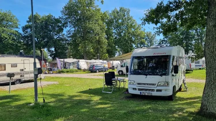 En campingplats med husvagnar och tält omgivna av träd. Flera fordon är parkerade på området.