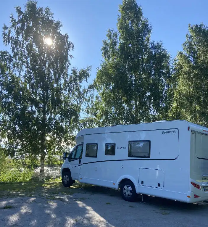 En husbil står parkerad på Ljusnefors camping, omgiven av grönska. Flera campingfordon syns i bakgrunden.