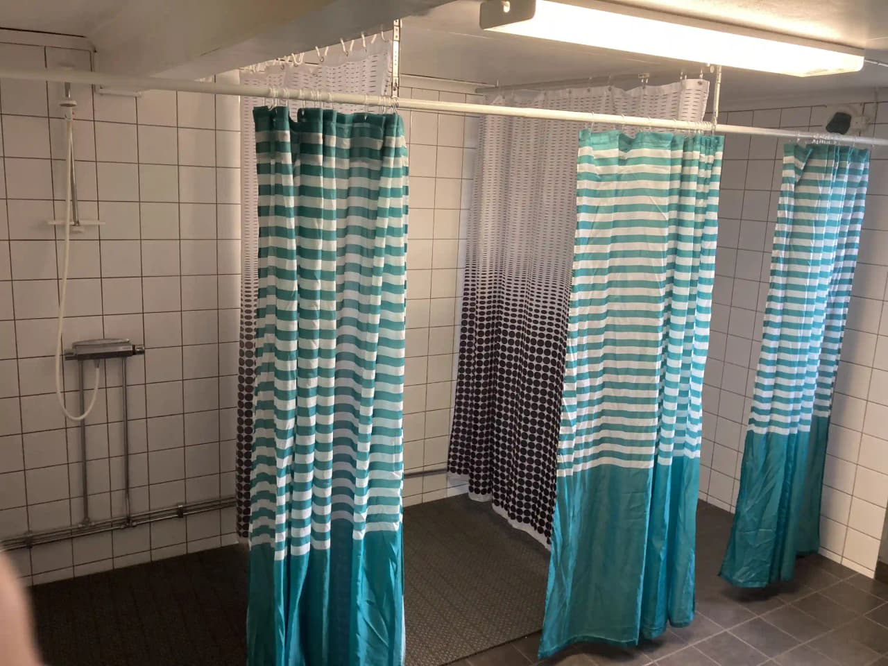 En ren och välorganiserad campingduschanläggning med duschdraperier och enkel inredningsdesign. Duschdraperierna fungerar som avskiljare och bidrar till en känsla av ordning och renlighet.