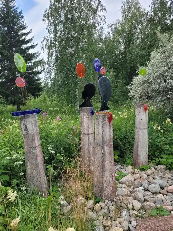 En grönskande campingmiljö med buskar och trädgårdskonst, omgiven av lummiga trädgårdar och en välskött gräsmatta i vårtid på Ånge Camping.