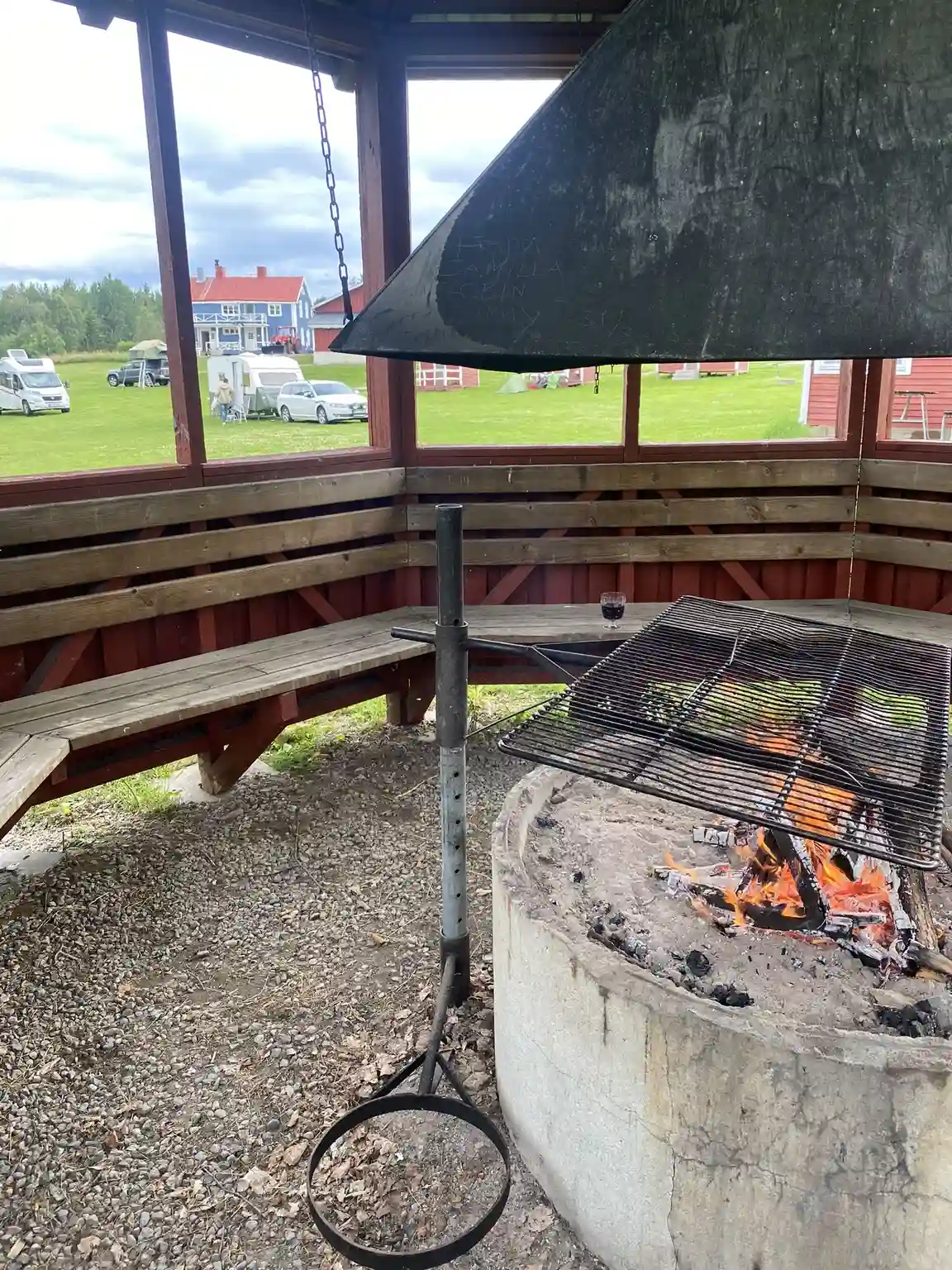 En picknickplats utomhus med träbord och bänkar under ett skuggande tak på Åmsele camping, omgiven av natur.
