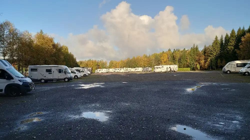 En vinterdag på Ullared camping med flera parkerade fordon, inklusive skåpbilar och SUV:ar, i en snötäckt parkeringsplats.