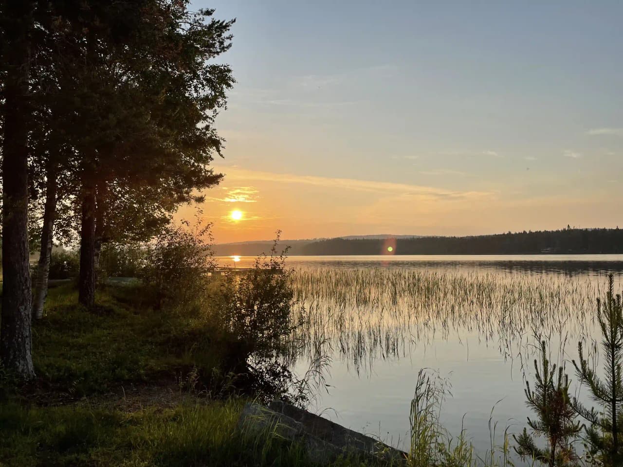 En somrig kvällsvy vid Fredrika Camping med en vidsträckt horisont över ett stilla vattendrag, omgärdat av naturligt grönskande landskap.