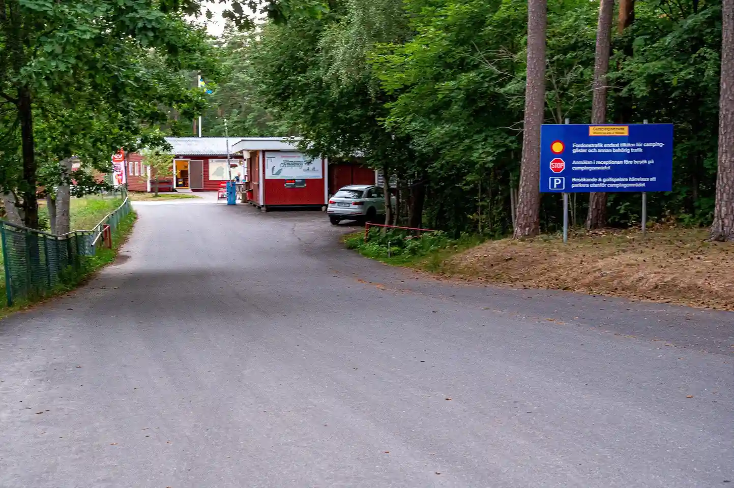 En asfalterad infart med vägskyltar som leder in till Värnamo camping. Träd omger vägen och skapar en naturskön miljö.