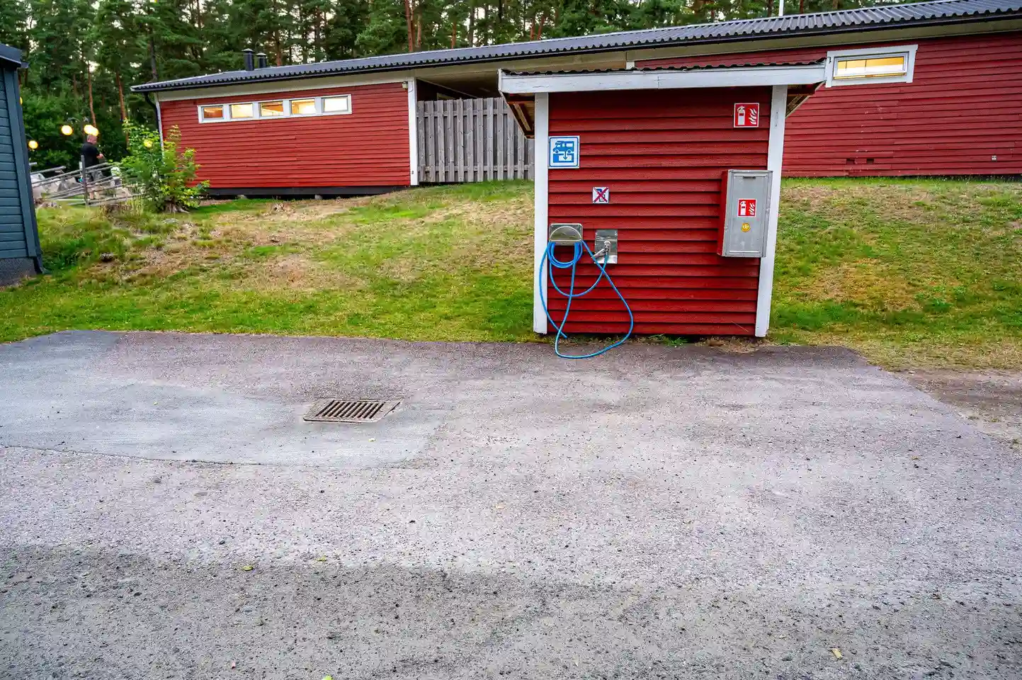 En asfalterad uppfart leder in på Värnamo Camping, där träd och buskar ramar in området. På sidan syns campingens byggnader med träpanel.