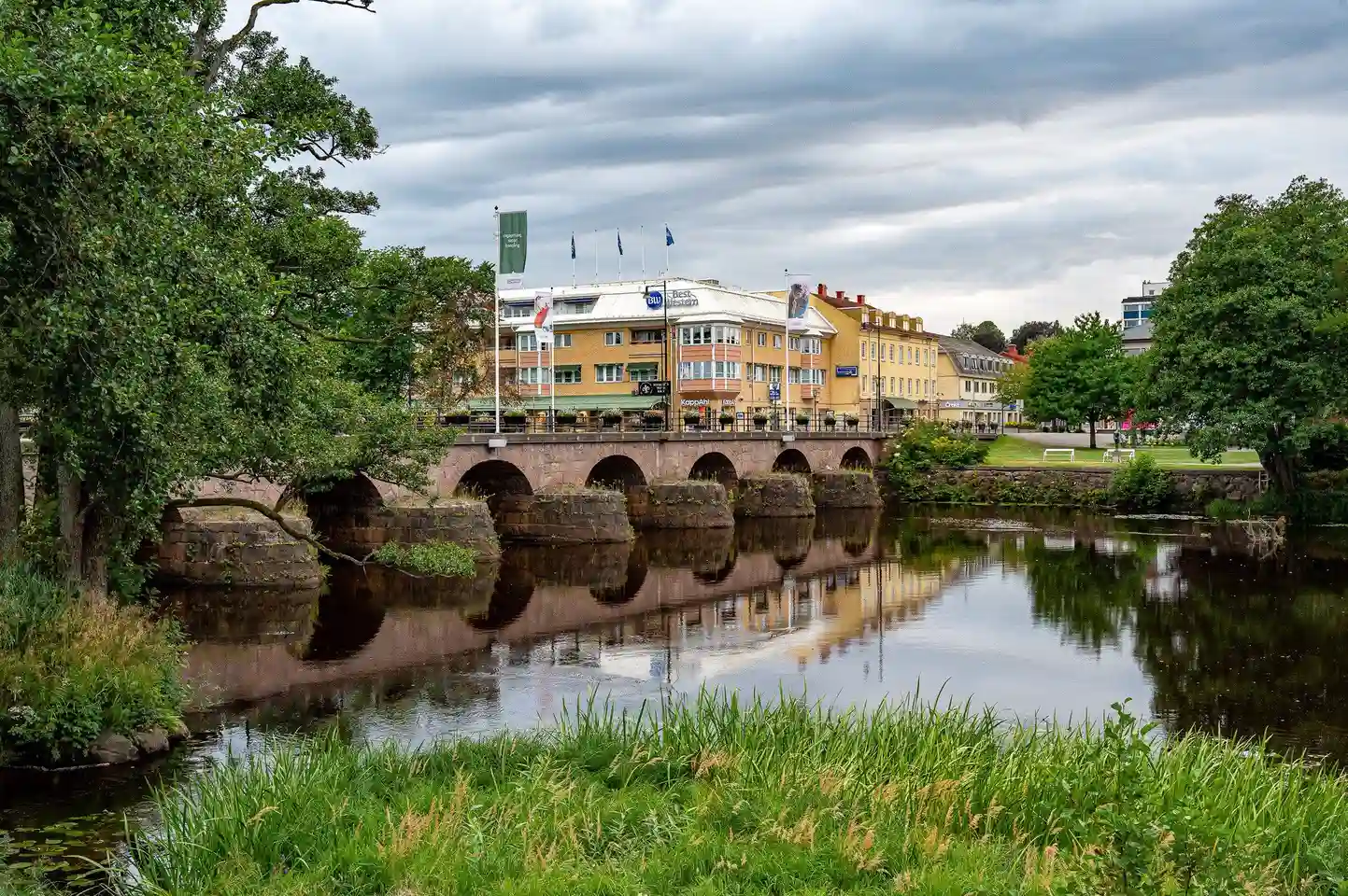 En betongbro över en lugn vattenkanal omgiven av grönska på Värnamo camping.