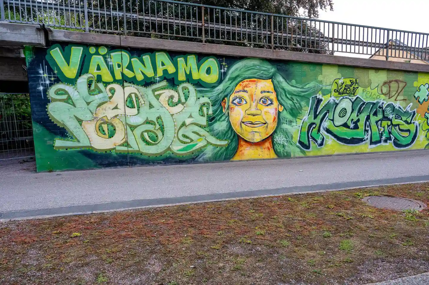 En stor muralmålning visas på en vägg vid Värnamo camping, med färgglada element och modern konststil som framhäver det kreativa uttrycket av street art och graffiti.