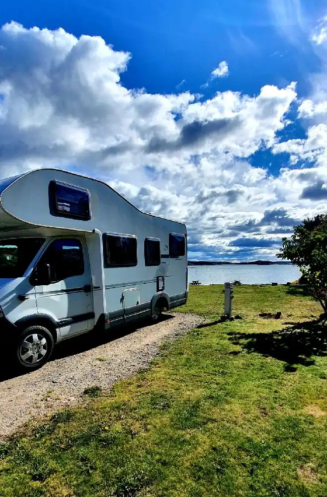 En campingplats med en husbil och flera husvagnar parkerade under en delvis molnig himmel.