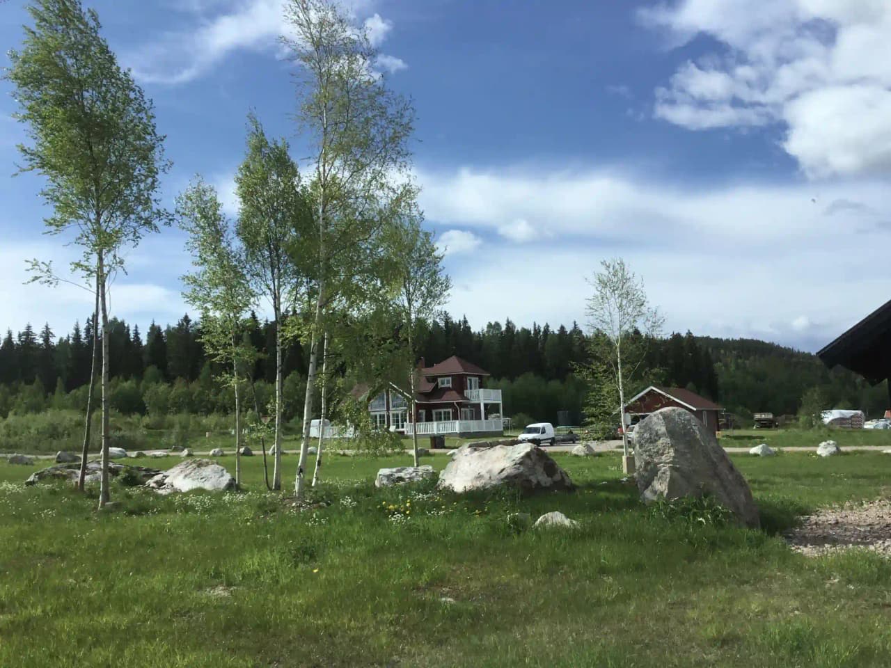 En grön äng i ett lantligt område i Dalarna, där en liten stuga omringas av vida grässlätter.