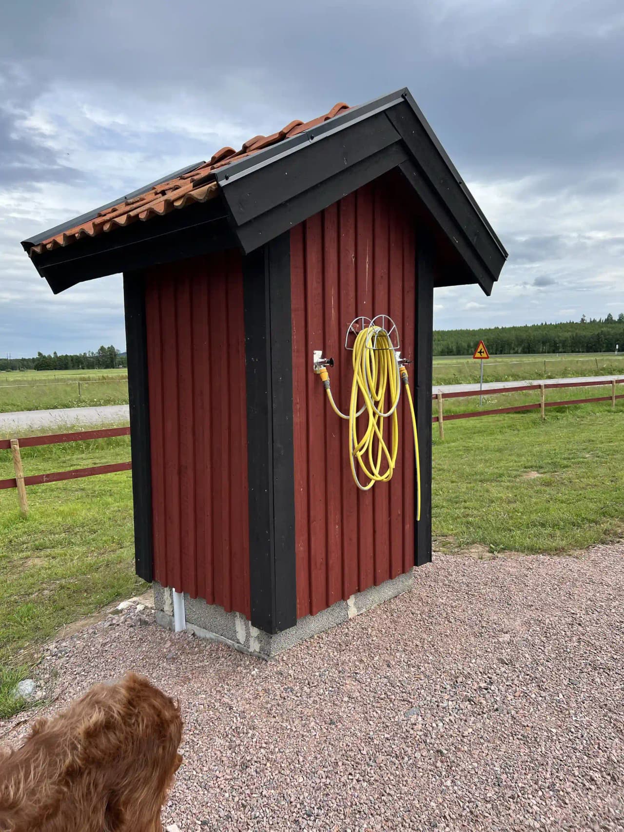 En liten träbod med trästängsel och gröna omgivningar vid Ställplats Dalarna, en avkopplande plats för besökare i naturskön miljö.