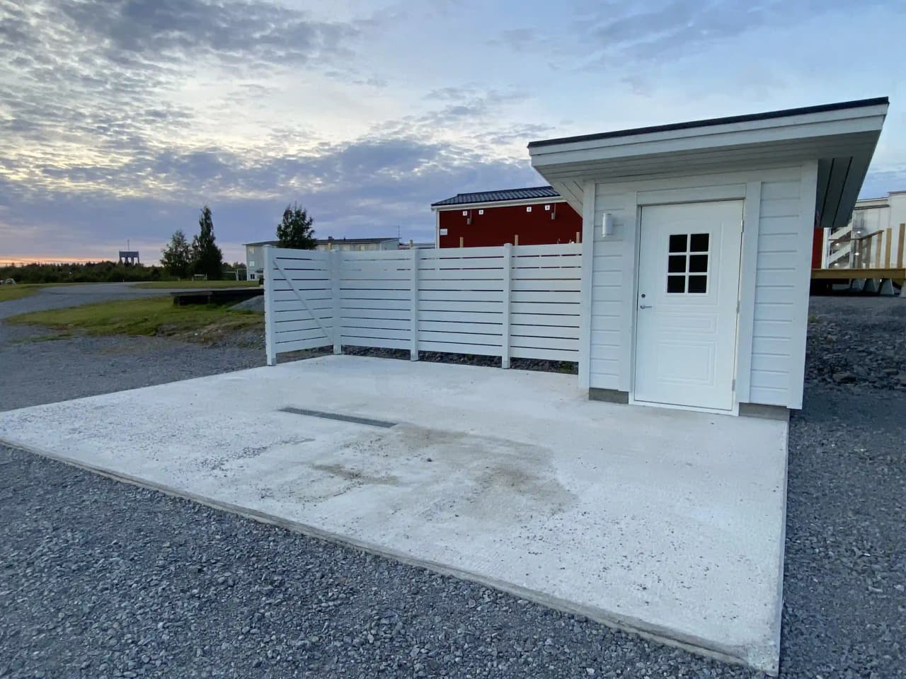 En modern byggnad med metallfasad och stora fönster, omgiven av gröna träd och en välskött trädgård.