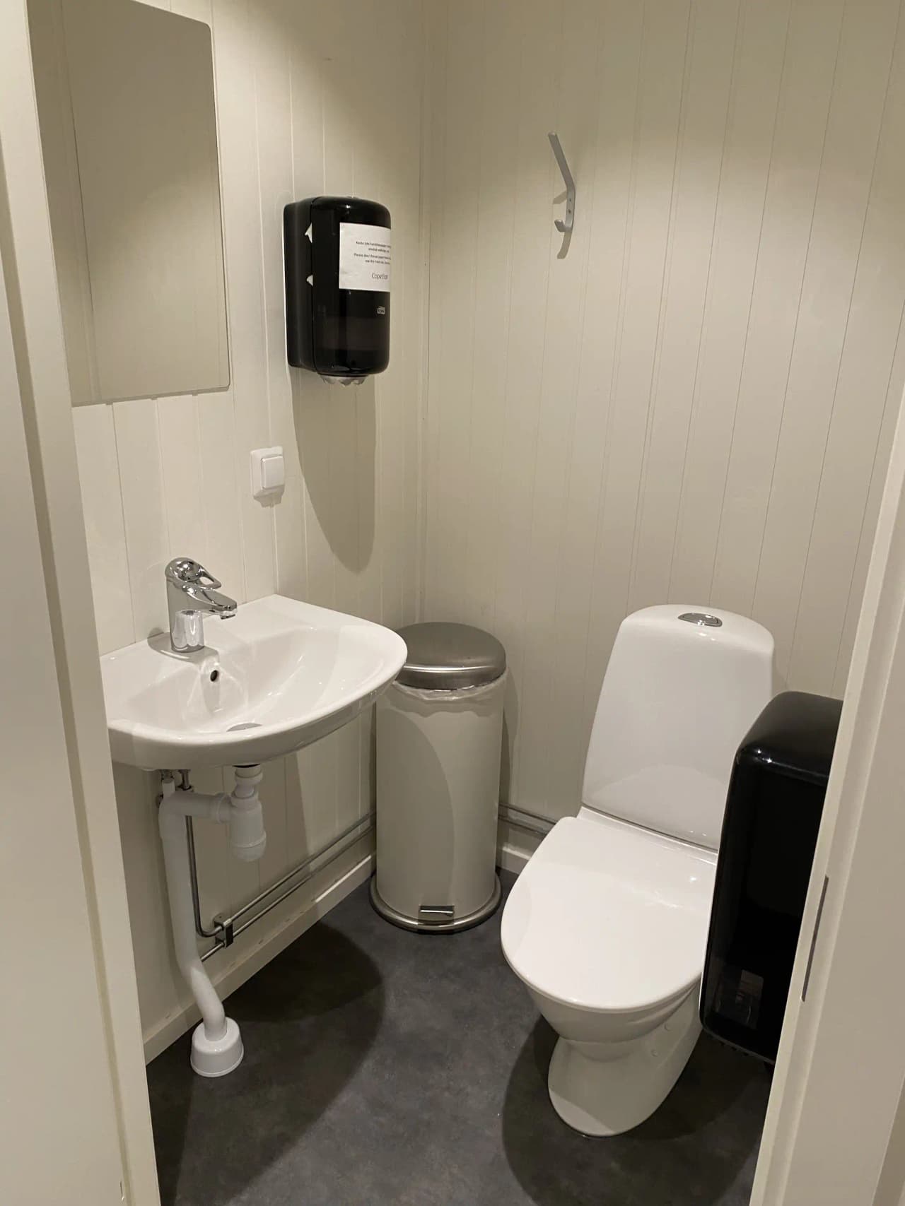 Ett modernt och stilrent badrum med en vit toalettstol, handfat och kaklat golv. Badrummets design utmärks av enkelhet och funktionalitet.