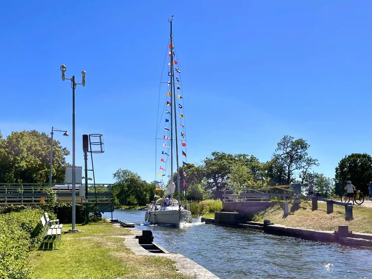 En stillsam vattenväg kantad av gröna träd och buskage, med en båt försiktigt förtöjd vid en träpåle. Vattnet speglar omgivningen och sträcker sig in i horisonten, vilket ger ett lugnande intryck av naturens skönhet i Jonsboda.