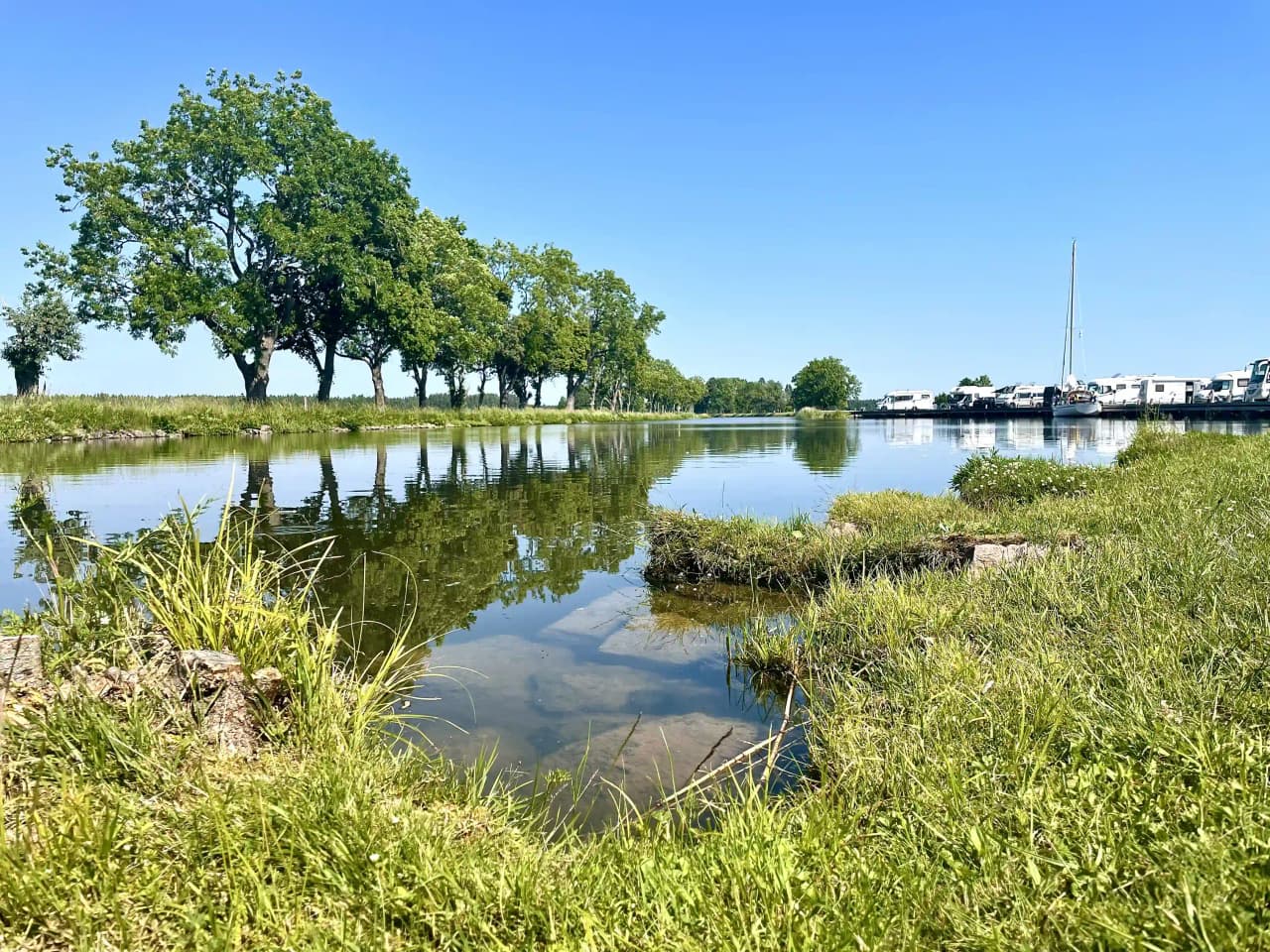En naturskön vy vid Jonsboda med en vattenkurs som rinner genom ett frodigt grönt landskap under en klarblå himmel.