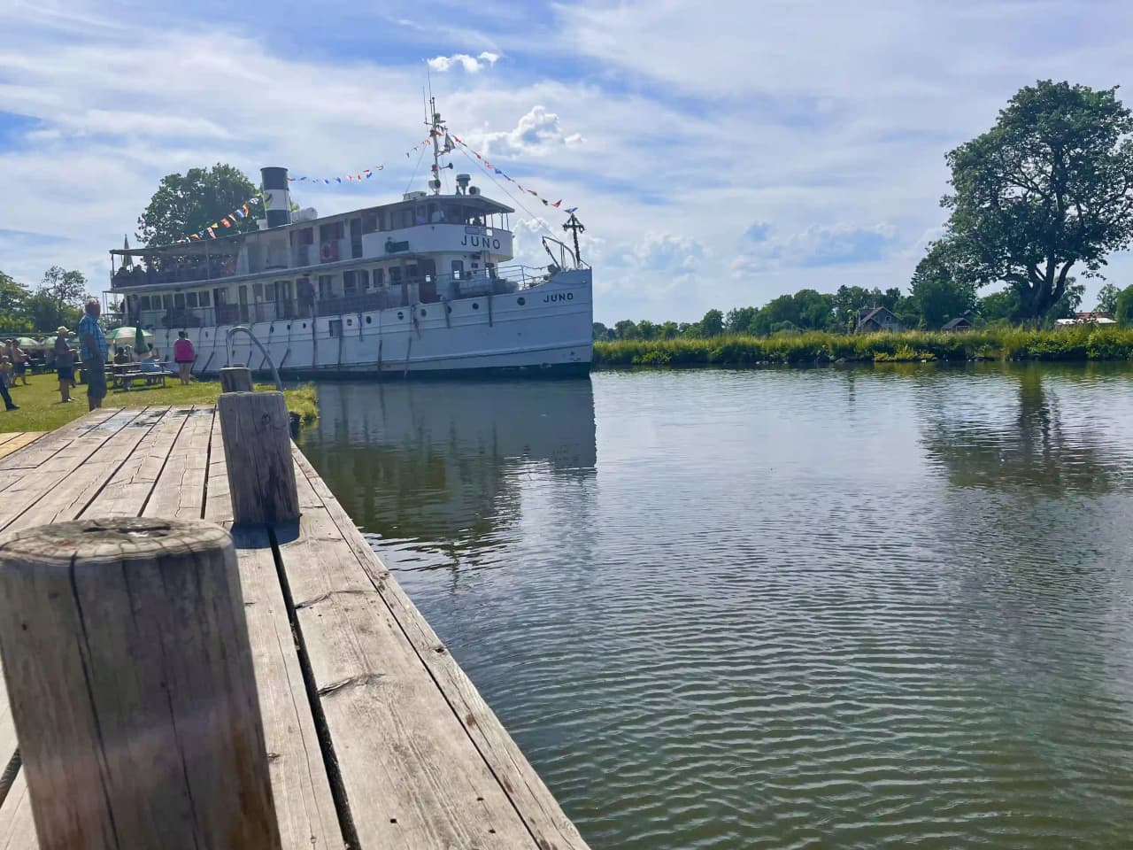 En somrig vy över en lugn vattenväg i Jonsboda med blå himmel och vita moln speglas i det stilla vattnet.