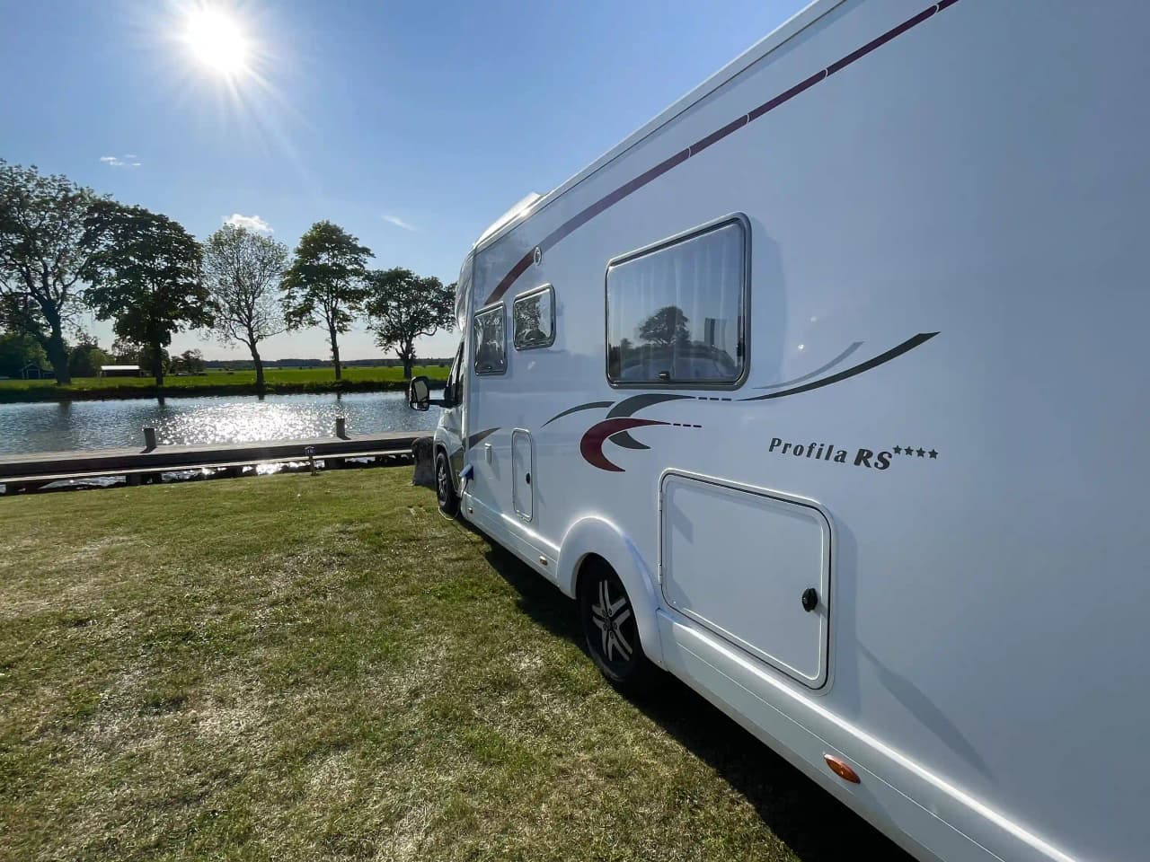 En vit husvagn med tillhörande bil står parkerad på en campingplats i Jonsboda, omgiven av grönska och träd.