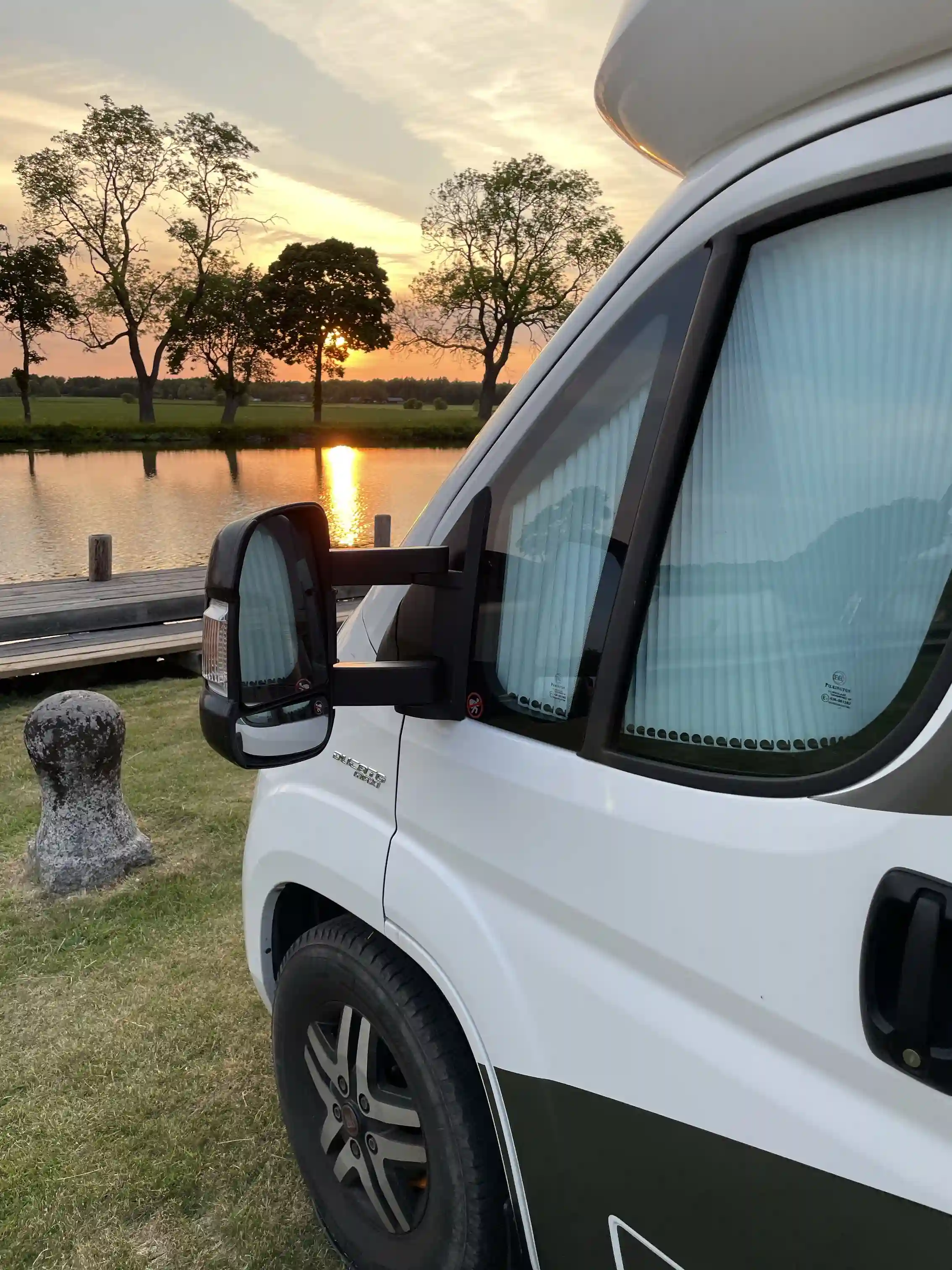 En ljus kommersiell skåpbil står parkerad på grusväg, omgiven av grönskande skog. Skåpbilens sidospeglar och dörrar är fullt synliga.