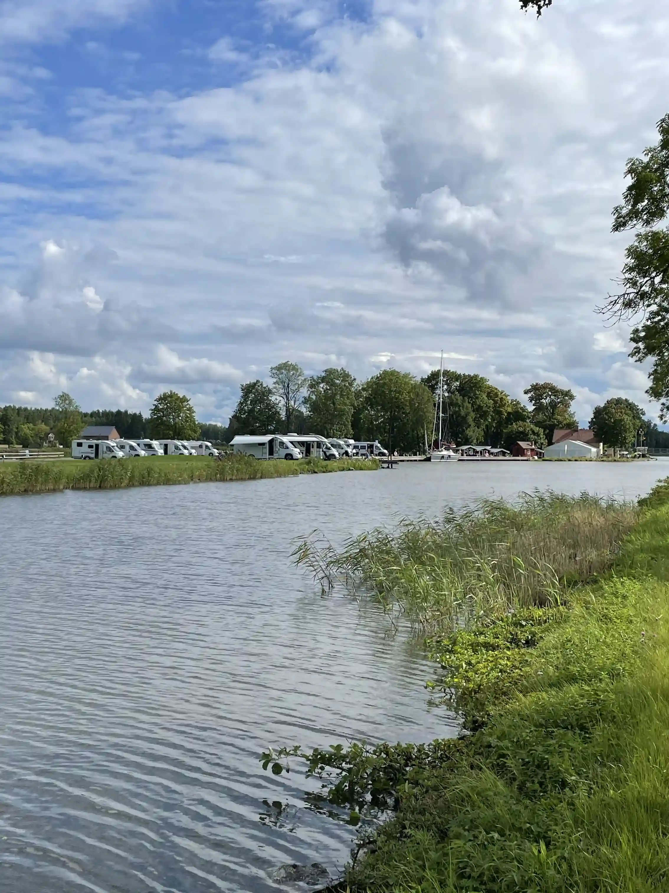 En lugn vattenspegel omgiven av grönskande sommarlandskap och molnprydd himmel, som skapar en fridfull atmosfär vid Jonsboda.