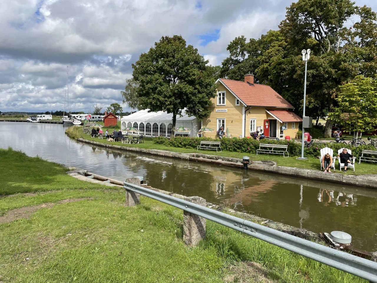 Bild av en lugn vattenväg med en liten stuga vid kanten. Vattnet omges av grönskande växtlighet och skapar en idyllisk och fridfull atmosfär vid besöksmålet Jonsboda.