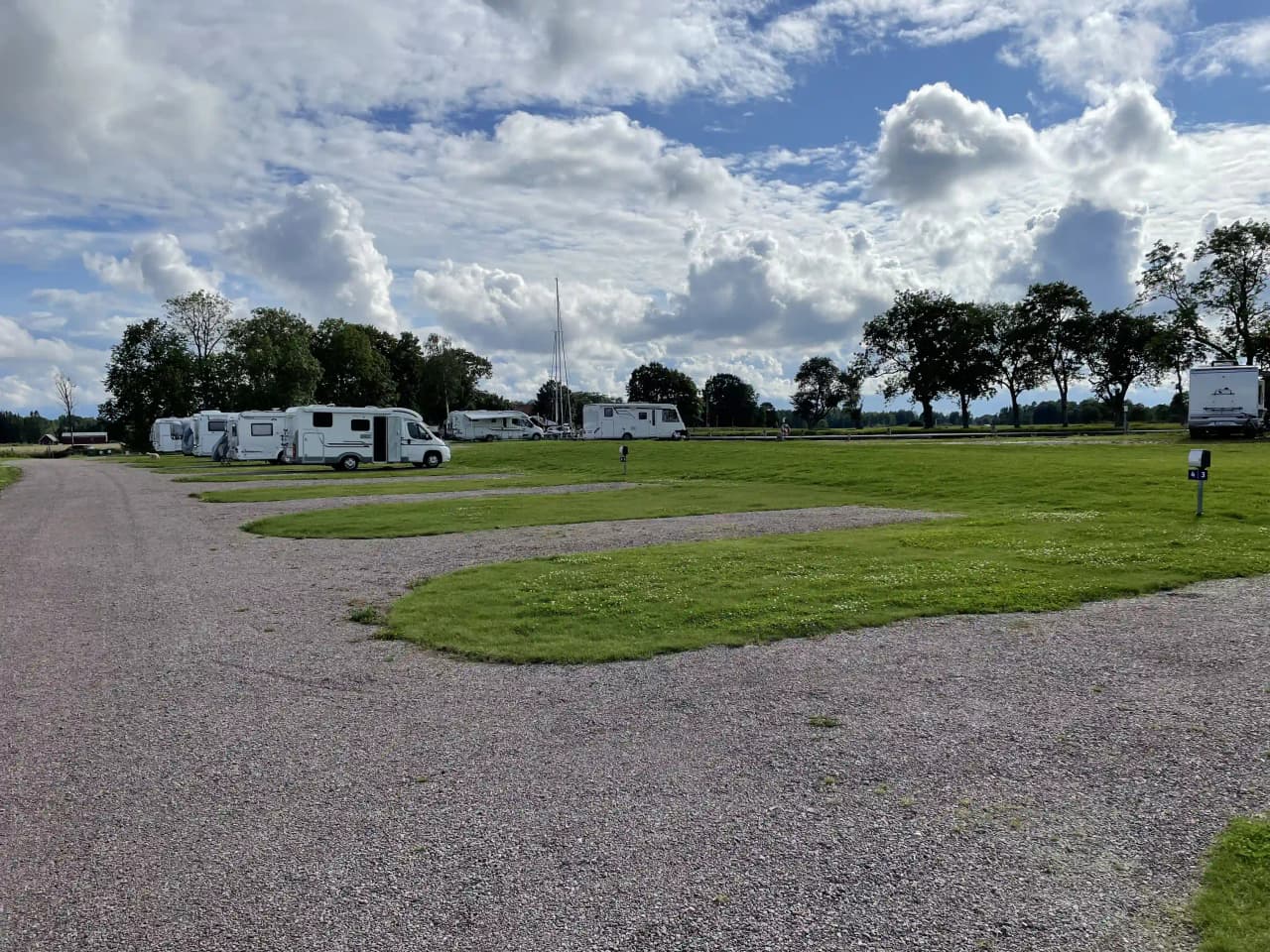 En husvagn står parkerad på en öppen gräsyta under en himmel med vita molnformationer.