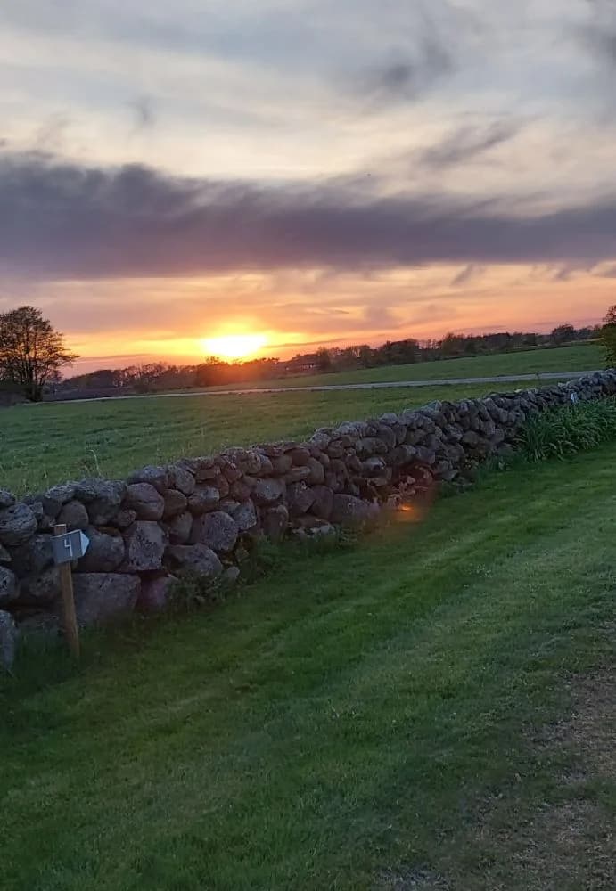 En solnedgång över ett öppet landskap vid Björkängs vandrarhem, med en vidsträckt himmel, moln och det dämpade ljuset från horisonten.