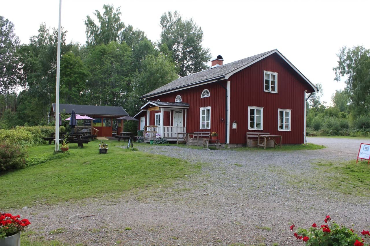 En pittoresk stuga på Älgå hembygdsgård omgiven av grönskande växter, med ett traditionellt tak och lantlig miljö.