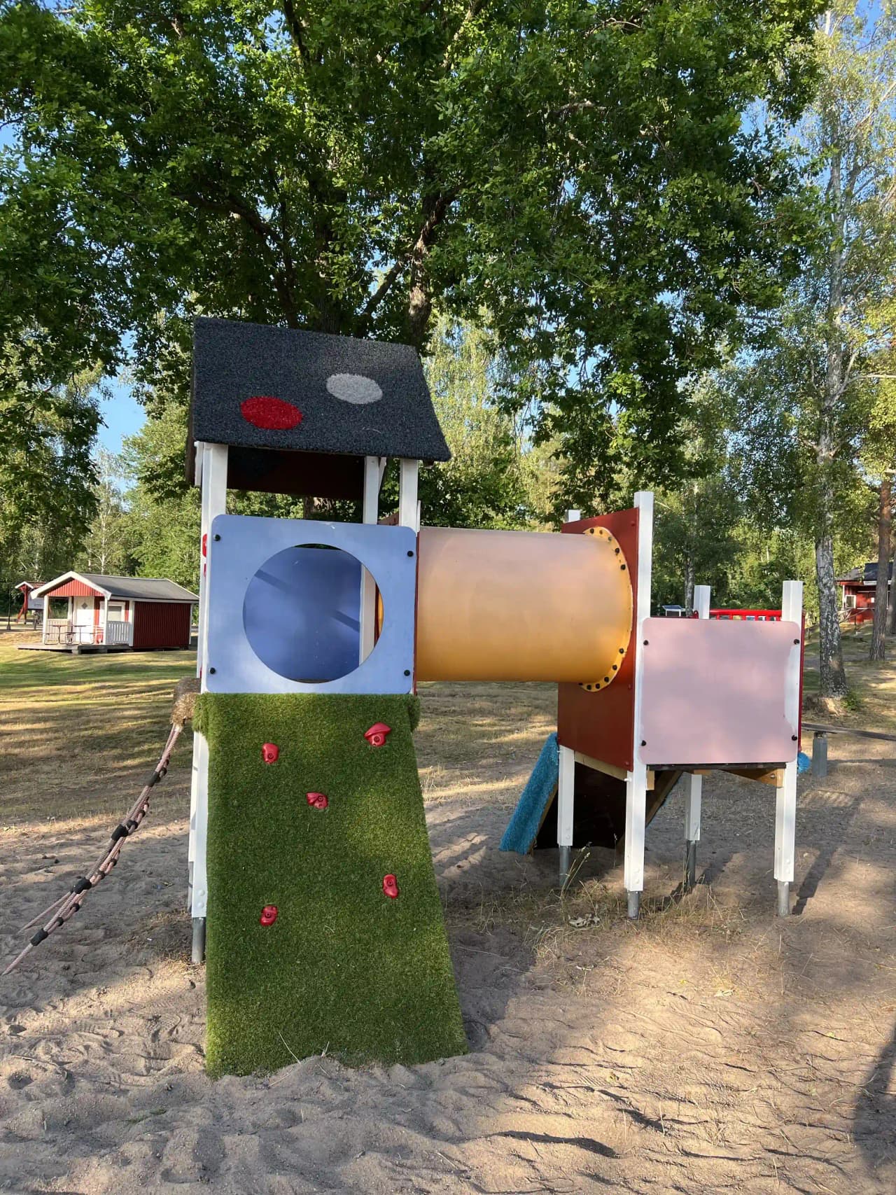 En lekplats vid gudingebadet med rutschkana och andra uteleksaker, omgiven av grönska och nära ett bostadsområde.