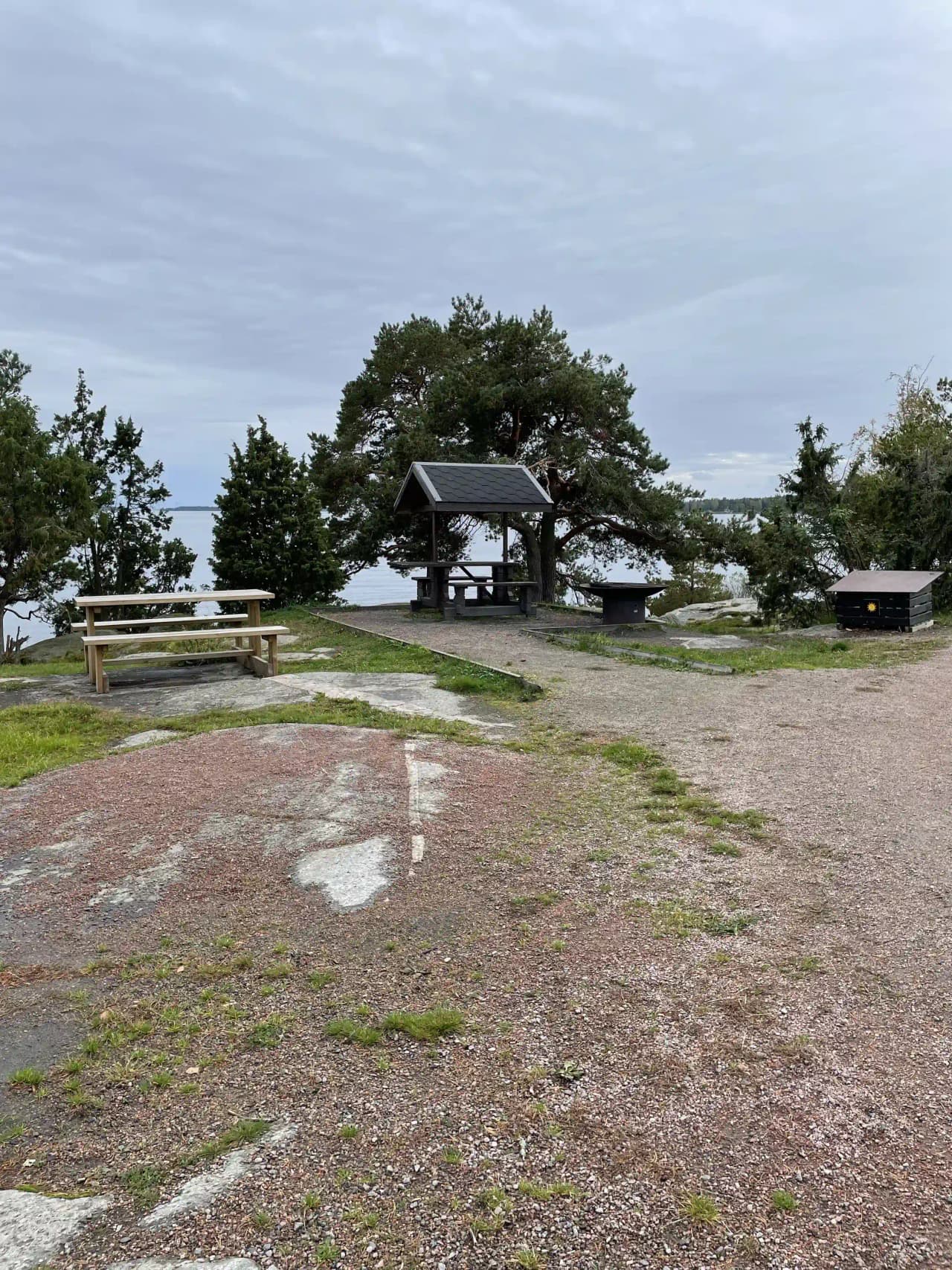 En solig dag vid Mösseberg camping med moln på himlen. Fokus på ett tält bredvid ett picknickbord och en utomhusbänk.